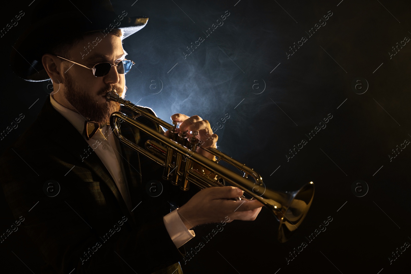 Photo of Professional musician playing trumpet on black background in smoke