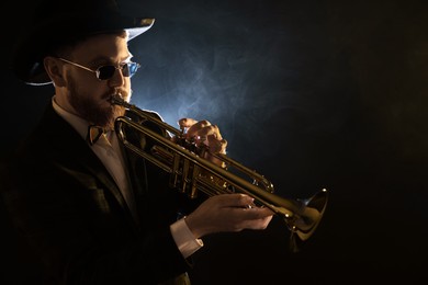 Photo of Professional musician playing trumpet on black background in smoke