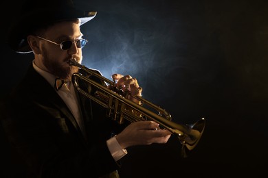 Professional musician playing trumpet on black background in smoke