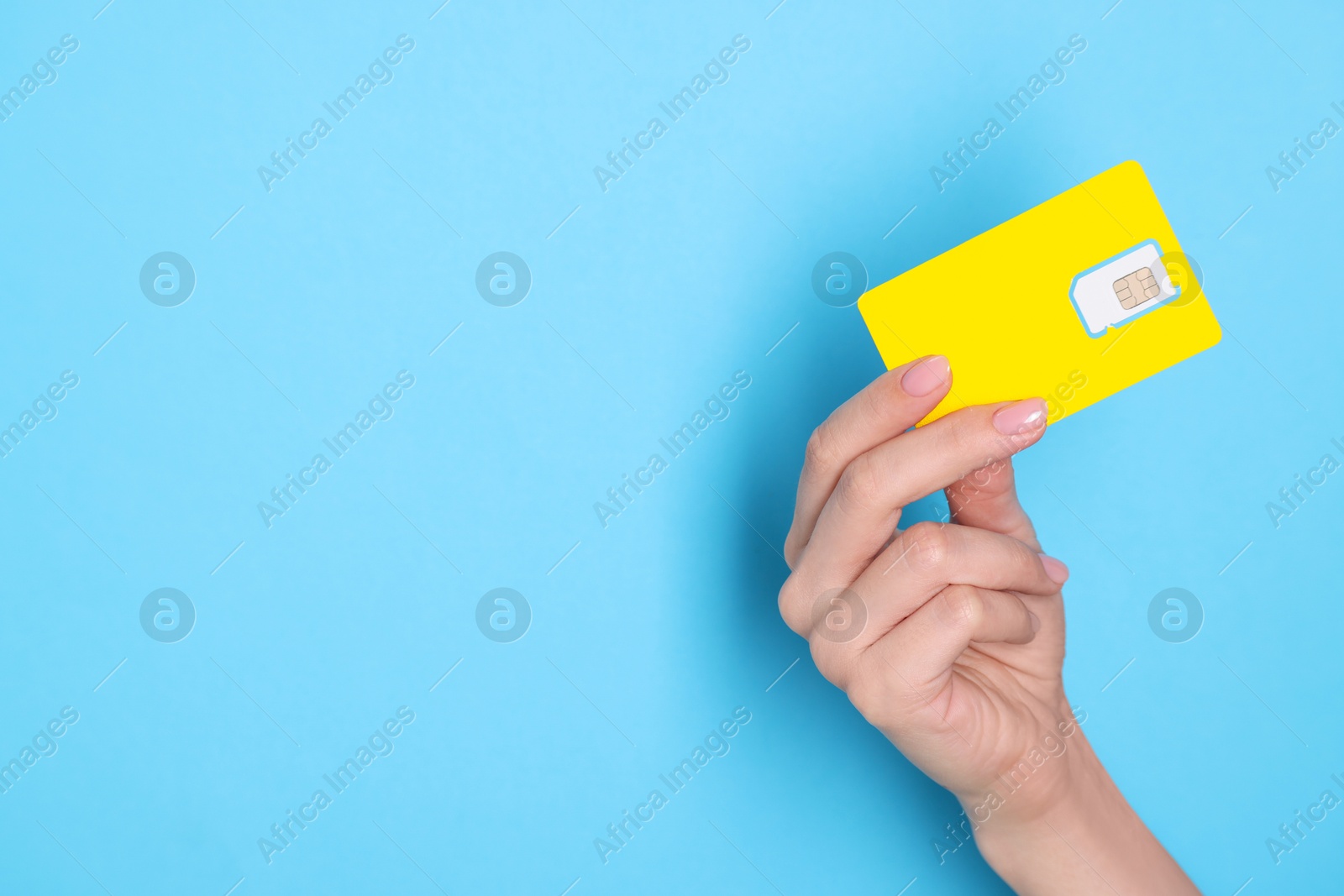 Photo of Woman holding SIM card on light blue background, closeup. Space for text