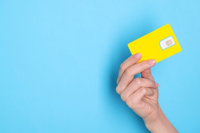 Photo of Woman holding SIM card on light blue background, closeup. Space for text