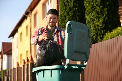 Photo of Man throwing trash bag full of garbage into bin outdoors