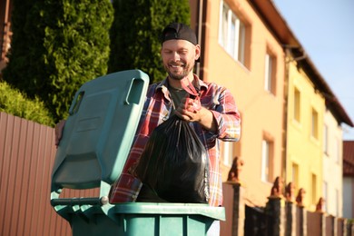 Photo of Man throwing trash bag full of garbage into bin outdoors, space for text