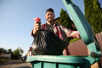 Photo of Man throwing trash bag full of garbage into bin outdoors, low angle view. Space for text