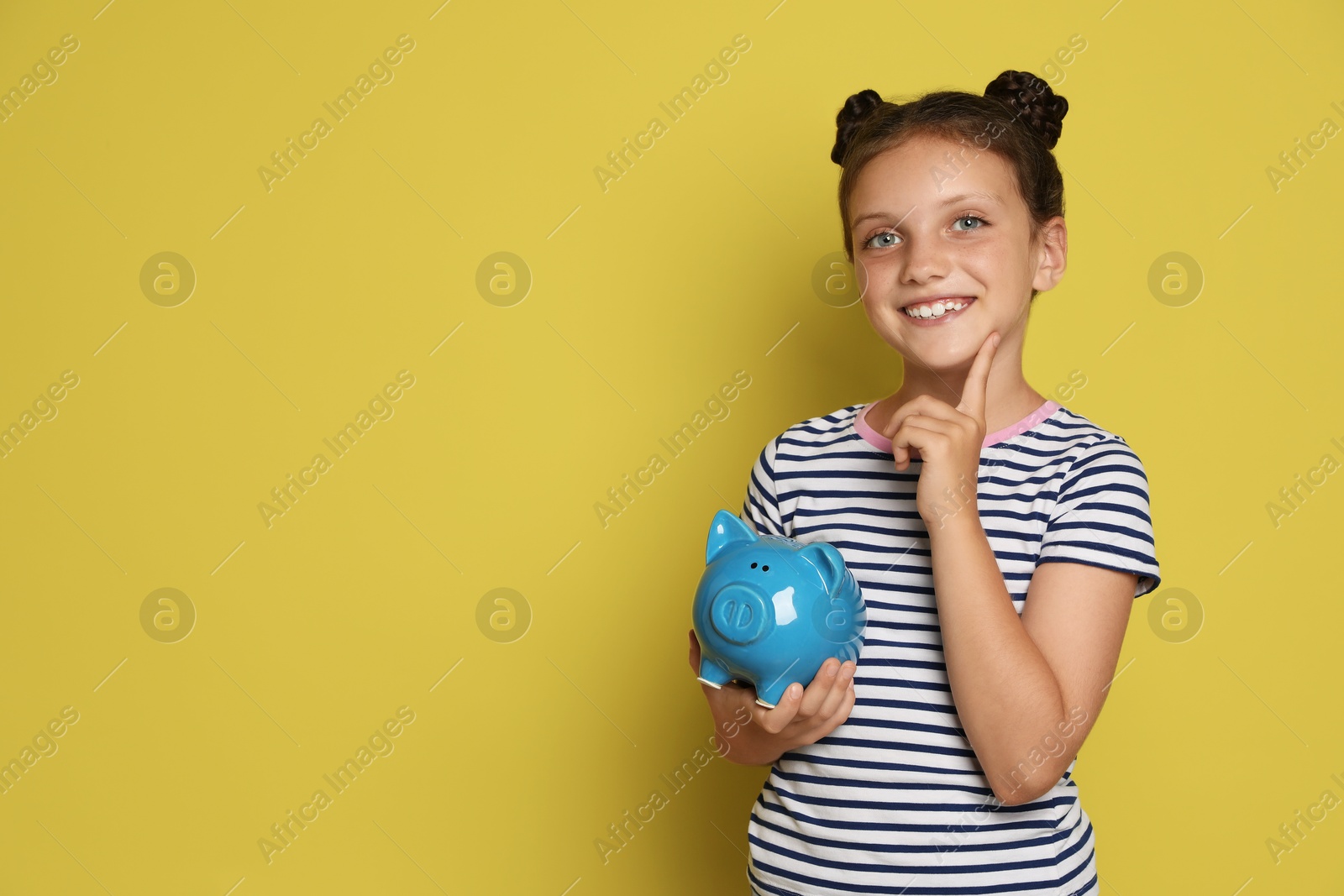 Photo of Pocket money. Cute girl with piggy bank on yellow background, space for text