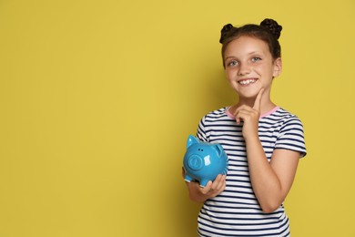 Pocket money. Cute girl with piggy bank on yellow background, space for text