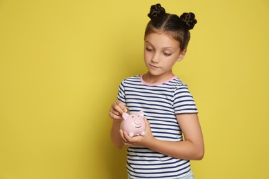 Photo of Pocket money. Cute girl putting coin into piggy bank on yellow background