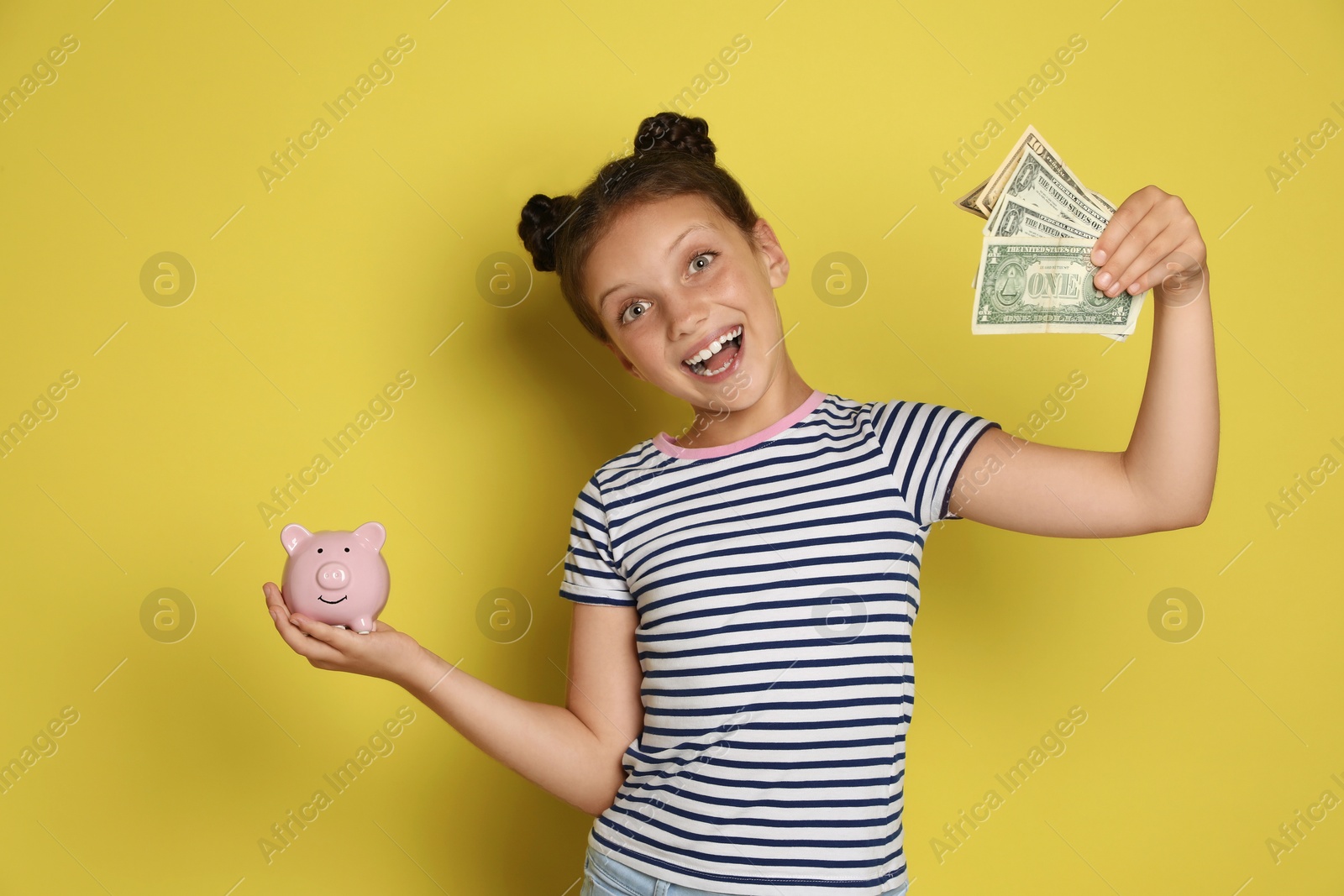 Photo of Pocket money. Cute girl with piggy bank and dollar banknotes on yellow background