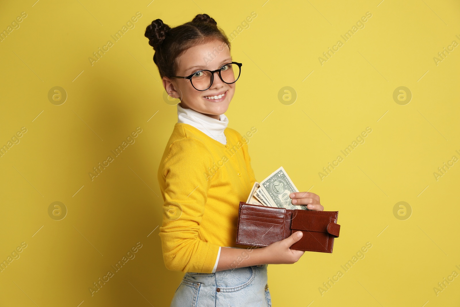 Photo of Pocket money. Cute girl with wallet and dollar banknotes on yellow background