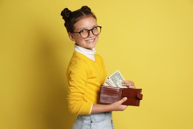 Photo of Pocket money. Cute girl with wallet and dollar banknotes on yellow background