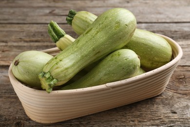 Photo of Raw green zucchinis in bowl on wooden table