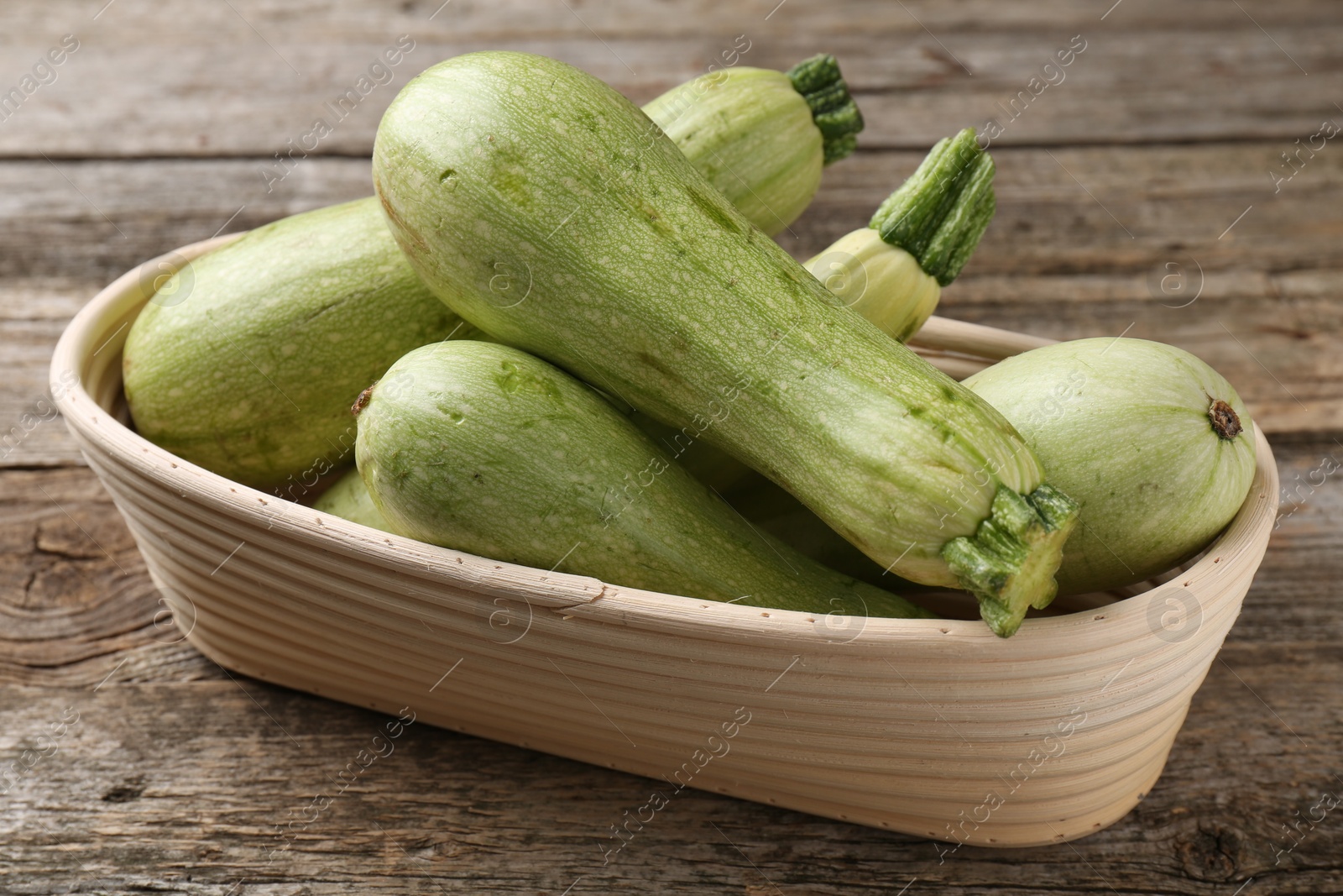 Photo of Raw green zucchinis in bowl on wooden table