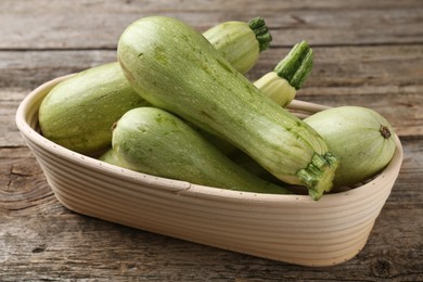 Photo of Raw green zucchinis in bowl on wooden table