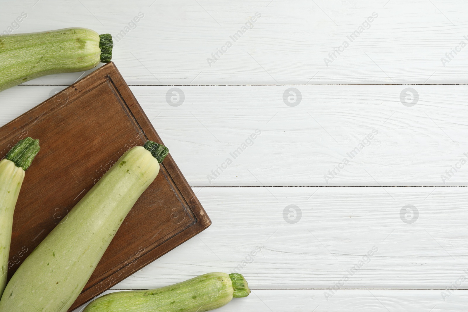 Photo of Raw green zucchinis on white wooden table, top view. Space for text