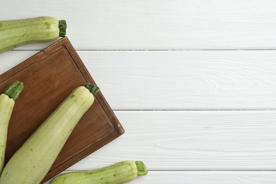 Photo of Raw green zucchinis on white wooden table, top view. Space for text