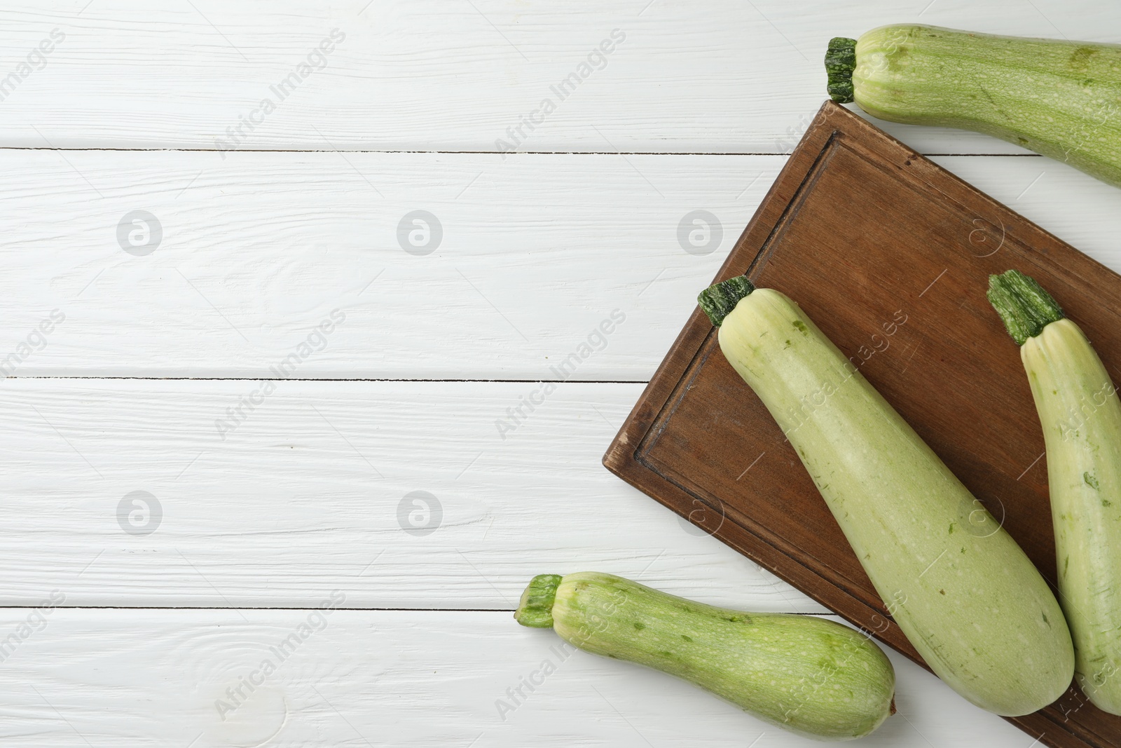 Photo of Raw green zucchinis on white wooden table, top view. Space for text