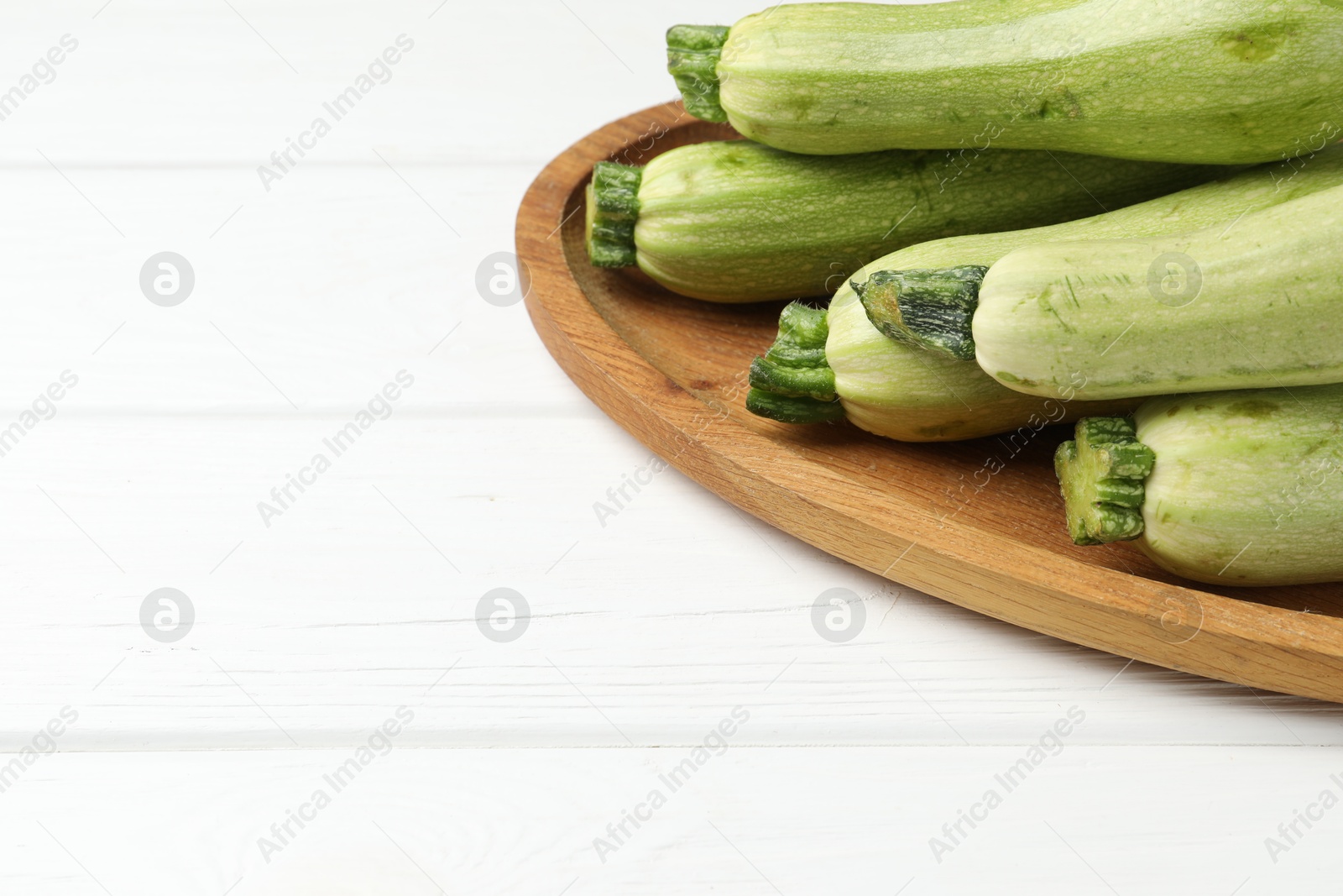 Photo of Raw green zucchinis on white wooden table, space for text