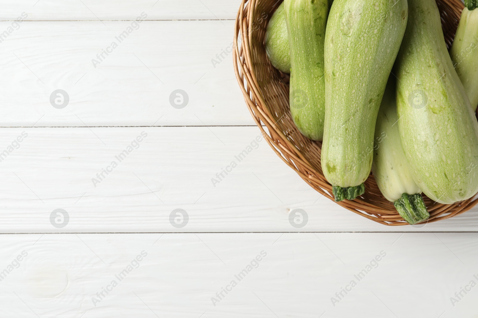 Photo of Raw green zucchinis on white wooden table, top view. Space for text