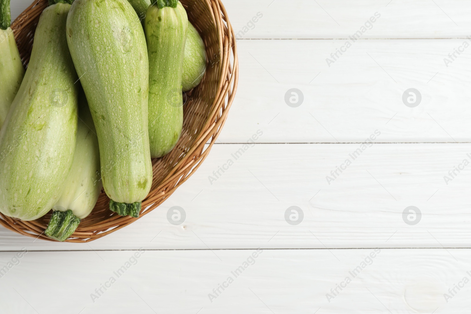 Photo of Raw green zucchinis on white wooden table, top view. Space for text