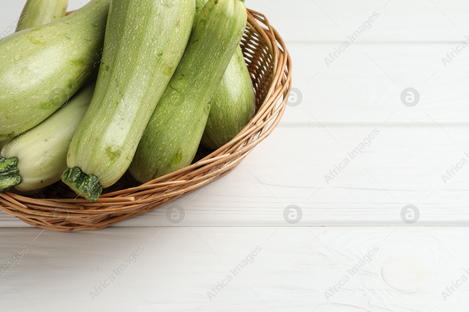 Photo of Raw green zucchinis on white wooden table, space for text