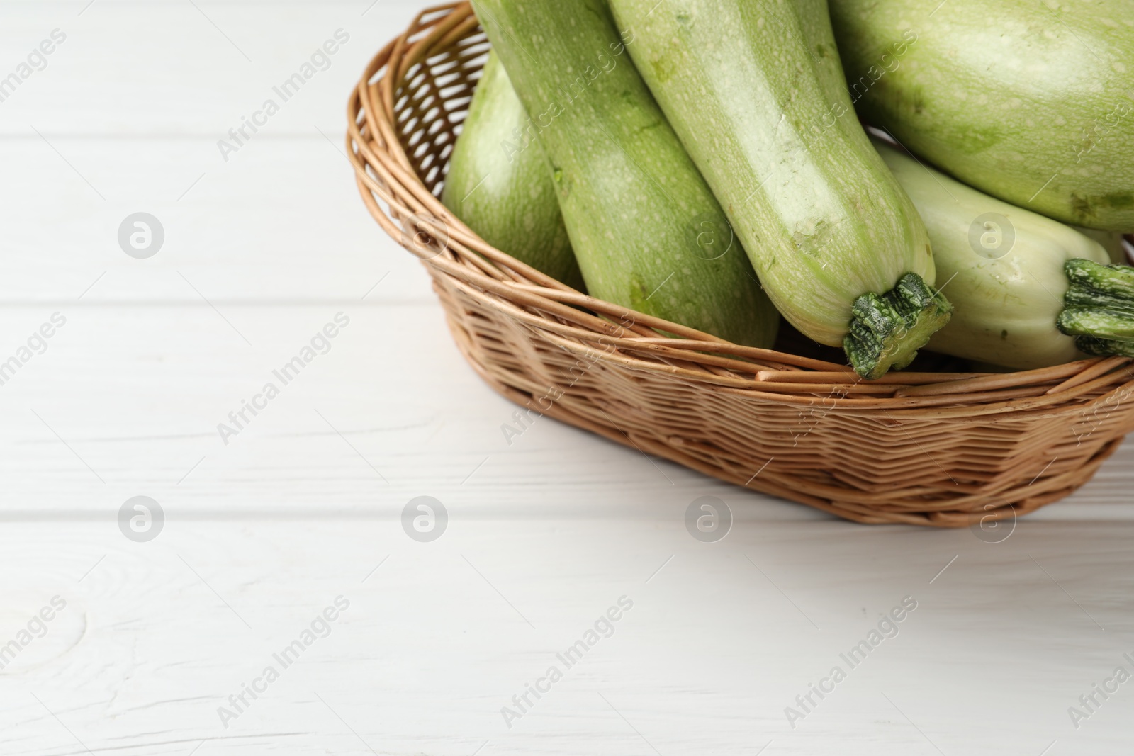 Photo of Raw green zucchinis on white wooden table, space for text