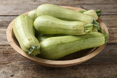 Photo of Raw green zucchinis in bowl on wooden table