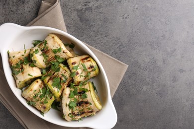 Photo of Tasty grilled zucchini rolls with parsley in dish on grey textured table, top view. Space for text