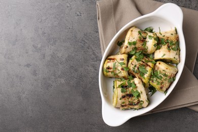 Tasty grilled zucchini rolls with parsley in dish on grey textured table, top view. Space for text