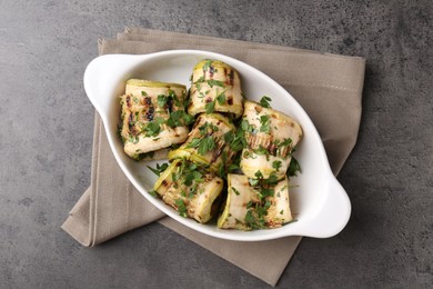 Photo of Tasty grilled zucchini rolls with parsley in dish on grey textured table, top view