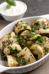 Tasty grilled zucchini rolls with parsley in dish on grey table, closeup