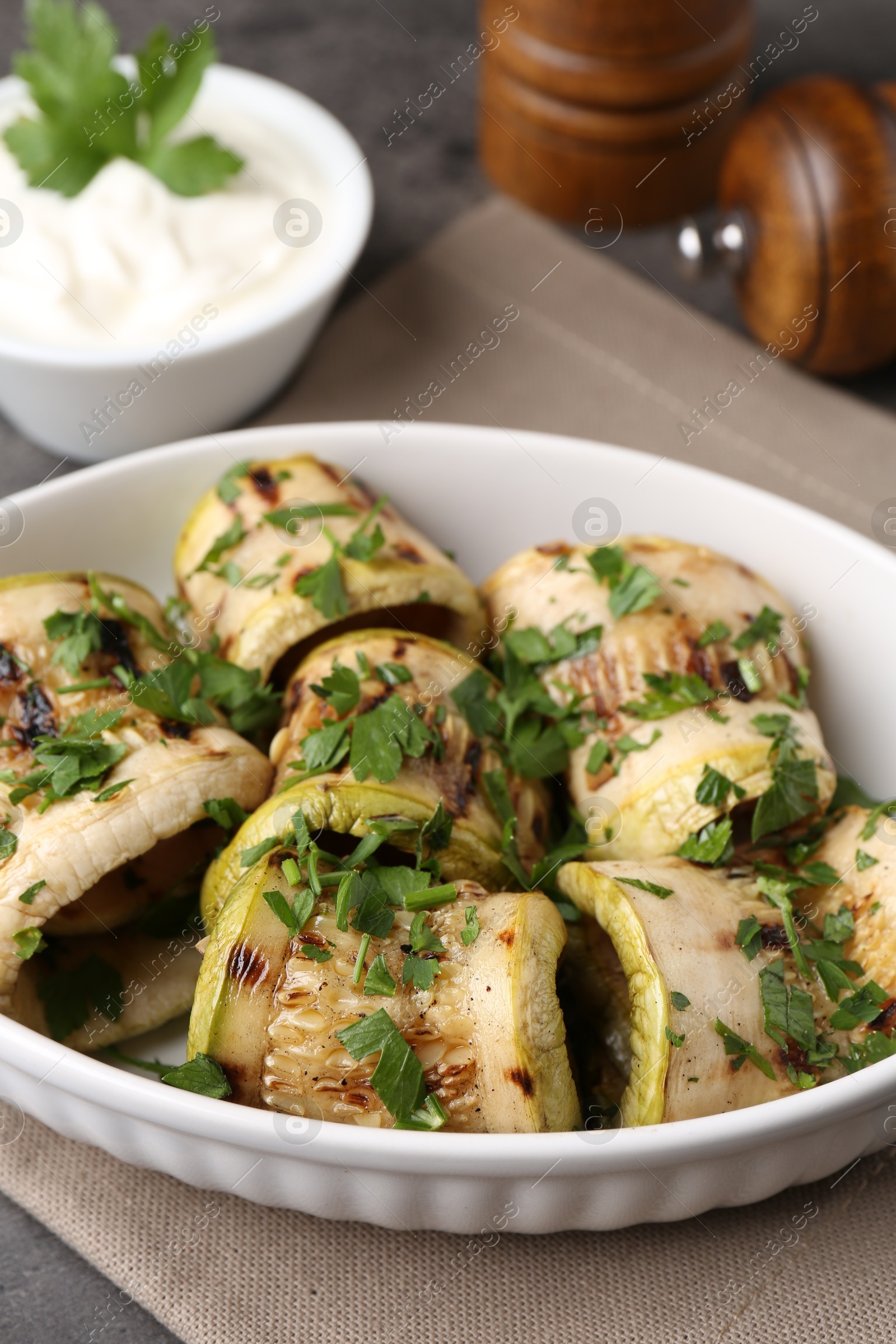 Photo of Tasty grilled zucchini rolls with parsley in dish on grey table