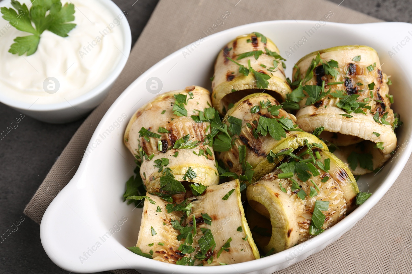 Photo of Tasty grilled zucchini rolls with parsley in dish served on grey table