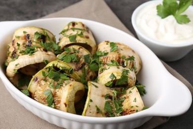 Tasty grilled zucchini rolls with parsley in dish served on grey table