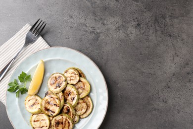 Photo of Tasty grilled zucchini slices served on grey textured table, flat lay. Space for text