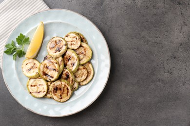 Photo of Tasty grilled zucchini slices with lemon and parsley on grey textured table, top view. Space for text