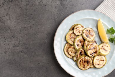 Photo of Tasty grilled zucchini slices with lemon and parsley on grey textured table, top view. Space for text