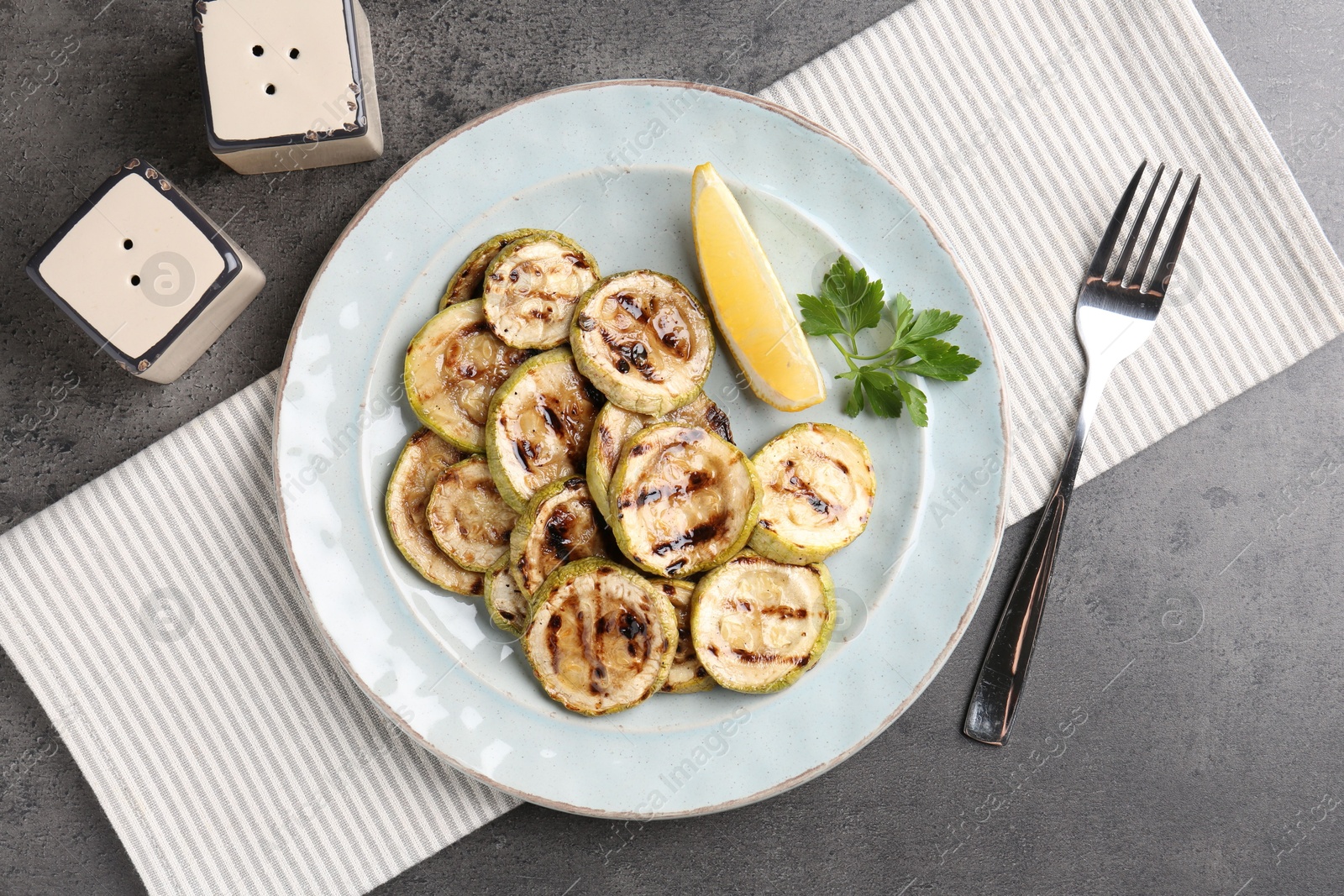 Photo of Tasty grilled zucchini slices served on grey textured table, flat lay