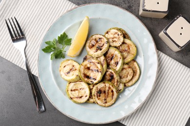 Photo of Tasty grilled zucchini slices served on grey textured table, flat lay