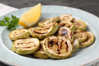 Photo of Tasty grilled zucchini slices with lemon and parsley on table, closeup