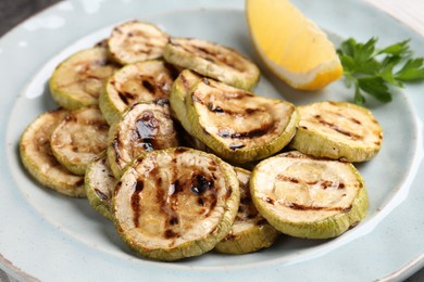 Photo of Tasty grilled zucchini slices with lemon and parsley on table, closeup