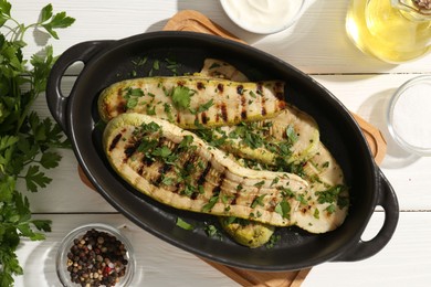 Tasty grilled zucchini slices served on white wooden table, flat lay