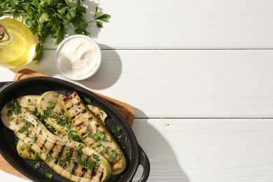 Tasty grilled zucchini slices served on white wooden table, flat lay. Space for text