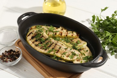 Photo of Tasty grilled zucchini slices in dish on white wooden table