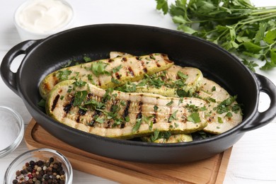 Photo of Tasty grilled zucchini slices in dish on white wooden table