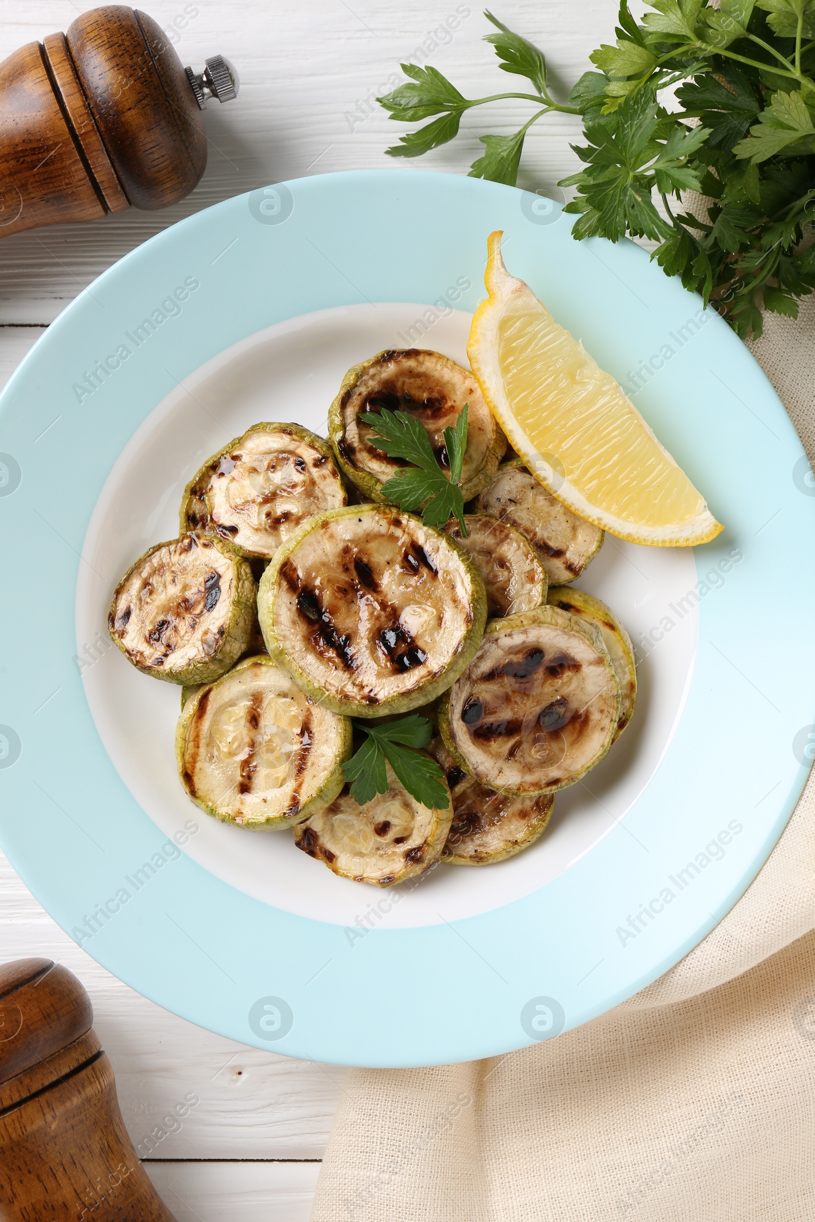 Photo of Tasty grilled zucchini slices with lemon and parsley on white wooden table, flat lay