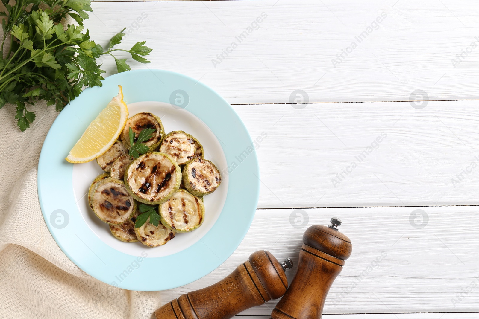 Photo of Tasty grilled zucchini slices with lemon and parsley on white wooden table, flat lay. Space for text