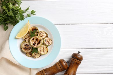 Photo of Tasty grilled zucchini slices with lemon and parsley on white wooden table, flat lay. Space for text