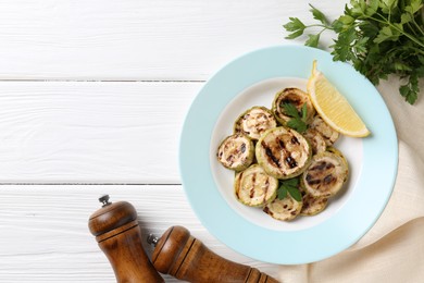 Photo of Tasty grilled zucchini slices with lemon and parsley on white wooden table, flat lay. Space for text