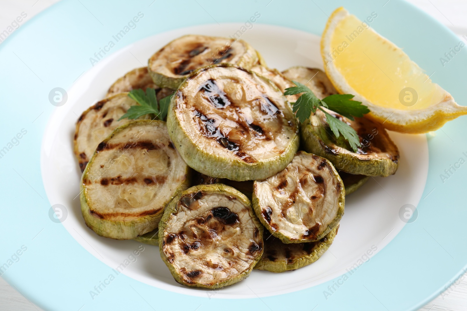 Photo of Tasty grilled zucchini slices with lemon and parsley on white table, closeup