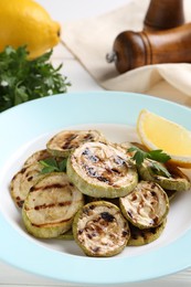 Photo of Tasty grilled zucchini slices with lemon and parsley on white table